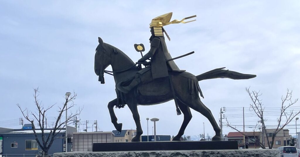 金色の兜をかぶった騎馬武将像の横からのシルエット