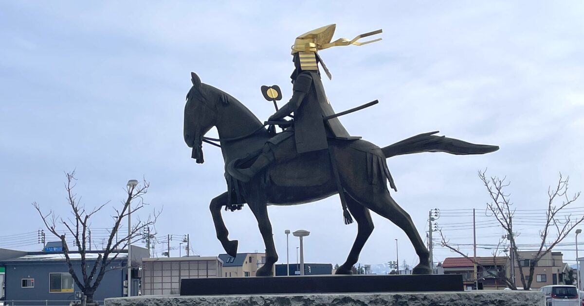 金色の兜をかぶった騎馬武将像の横からのシルエット