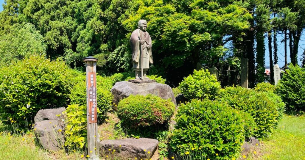 緑に囲まれた僧侶像と石碑が立つ公園の風景