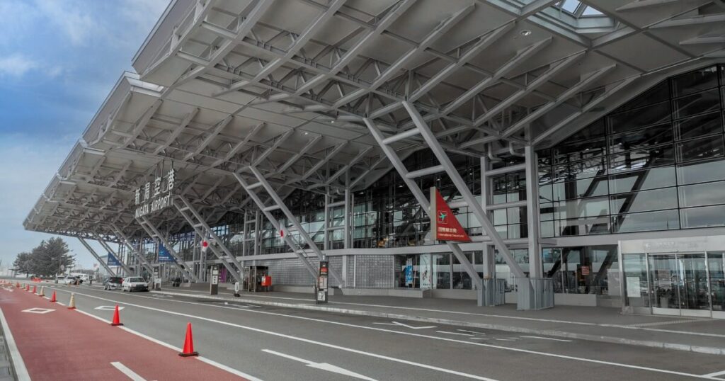 新潟空港のモダンな外観と送迎車両が並ぶ出発エリア