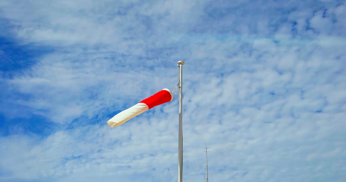 晴天の空にたなびく赤白の吹き流しと風向確認用ポール
