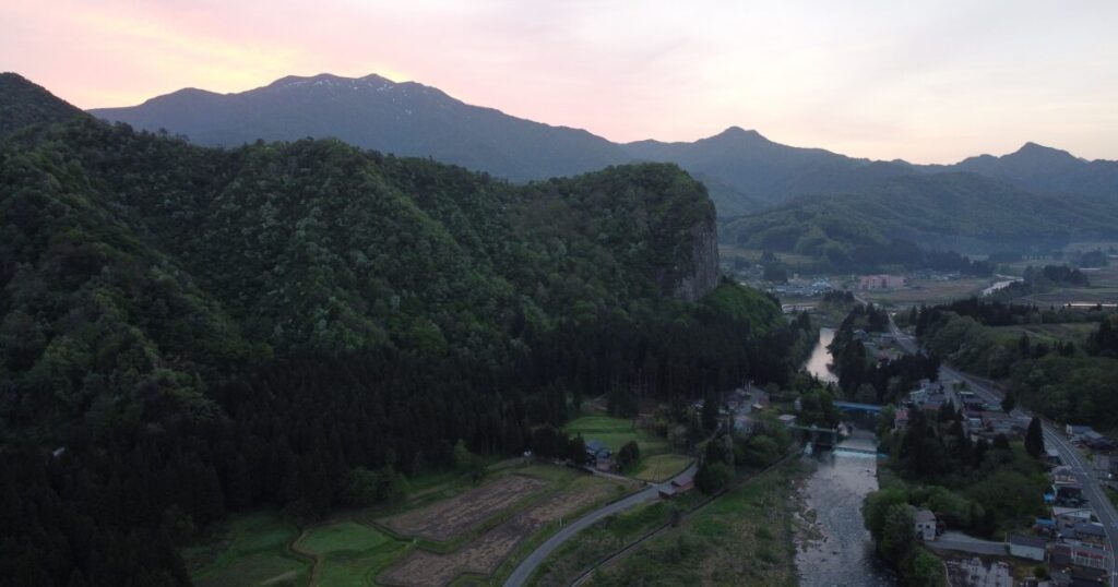 夕暮れに染まる山と川と町並みの航空写真