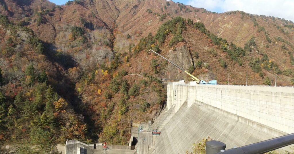 秋の山々に囲まれた大規模なコンクリートダムの景観